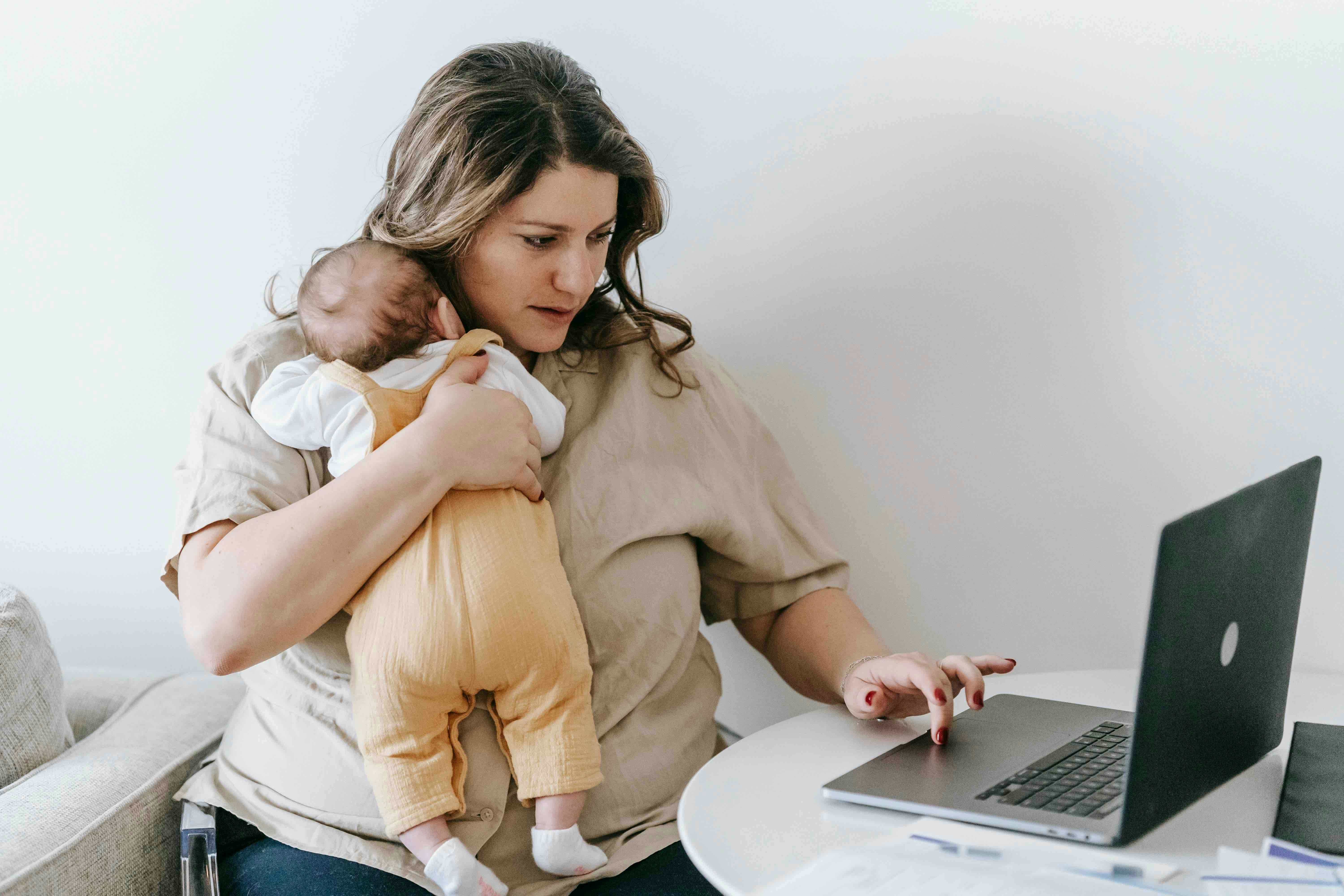 Mor som holder sitt barn samtidig som hun mottar teknisk fjernhjelp på datamaskinen